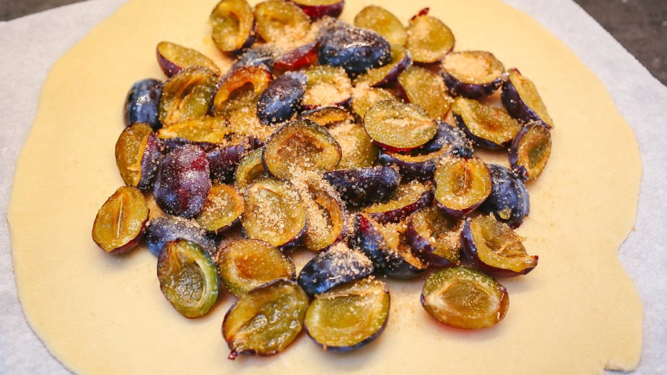 Vypekockované a přepůlené švestky nahrneme doprostřed koláče a rozprostřeme