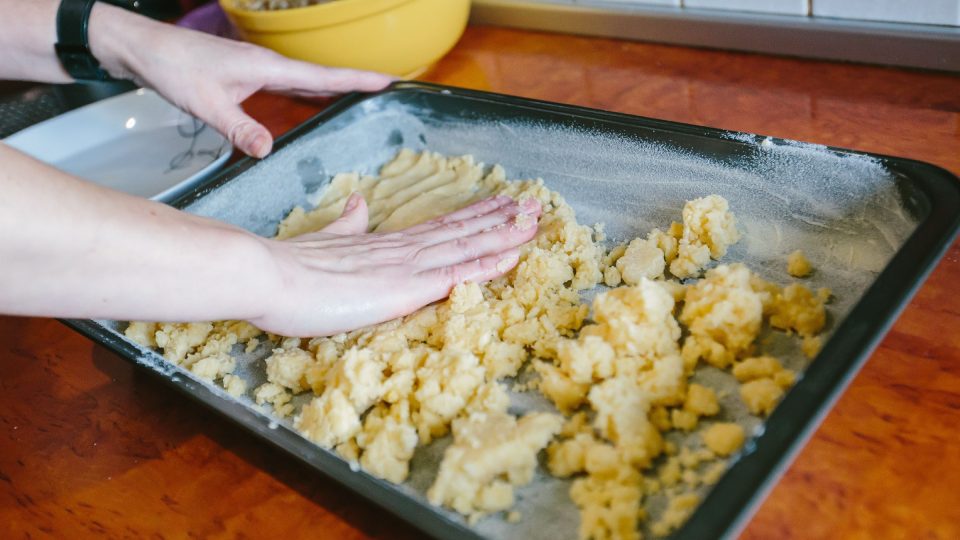 Část drobenkové směsi přesuneme na plech, pro lehčí kladení na plech pomůže namočit si ruce do vody