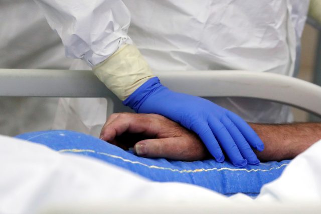 Zdravotník drží za ruku pacienta s koronavirem na jednotce intenzivní péče | foto: David W. Cerny,  Reuters